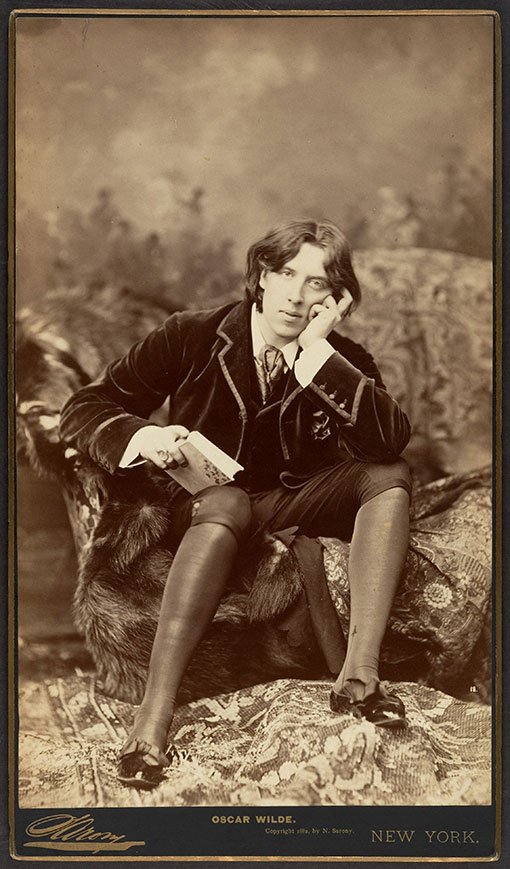 Full-length studio portrait of Oscar Wilde, seated.