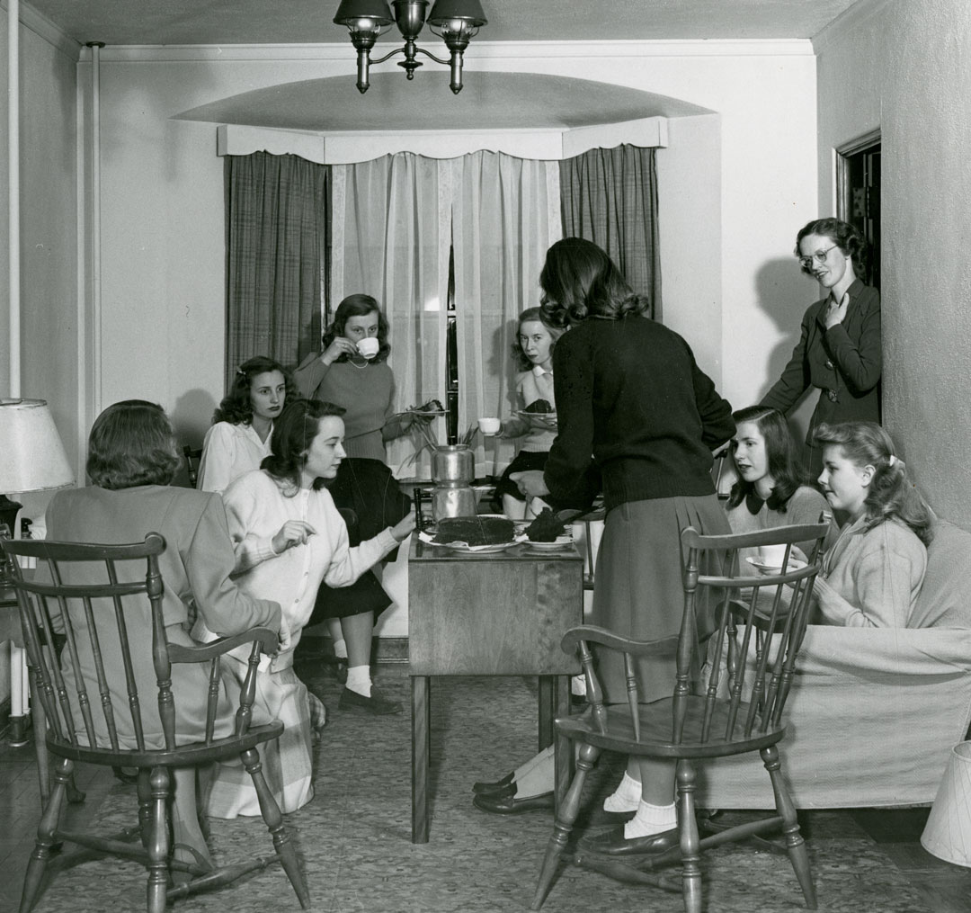 A black and white photograph of several women having tea in a parlor.