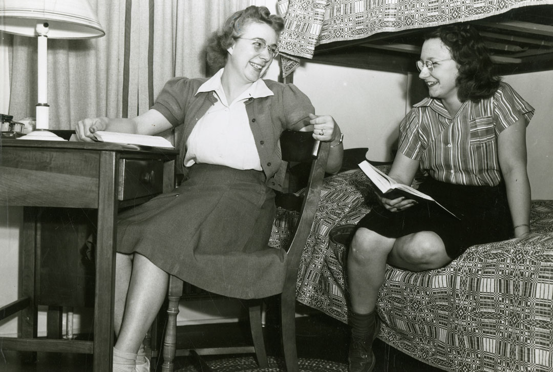 A black and white photograph of two women in a dorm room.