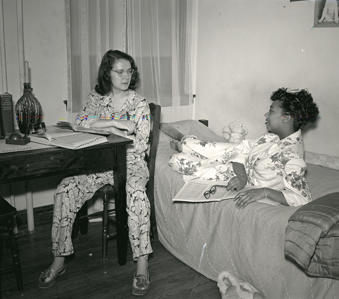 A black and white photo of two women in a dorm room
