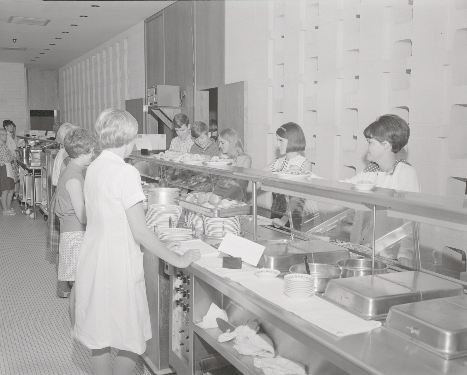 A black and white image of people getting food from a buffet line