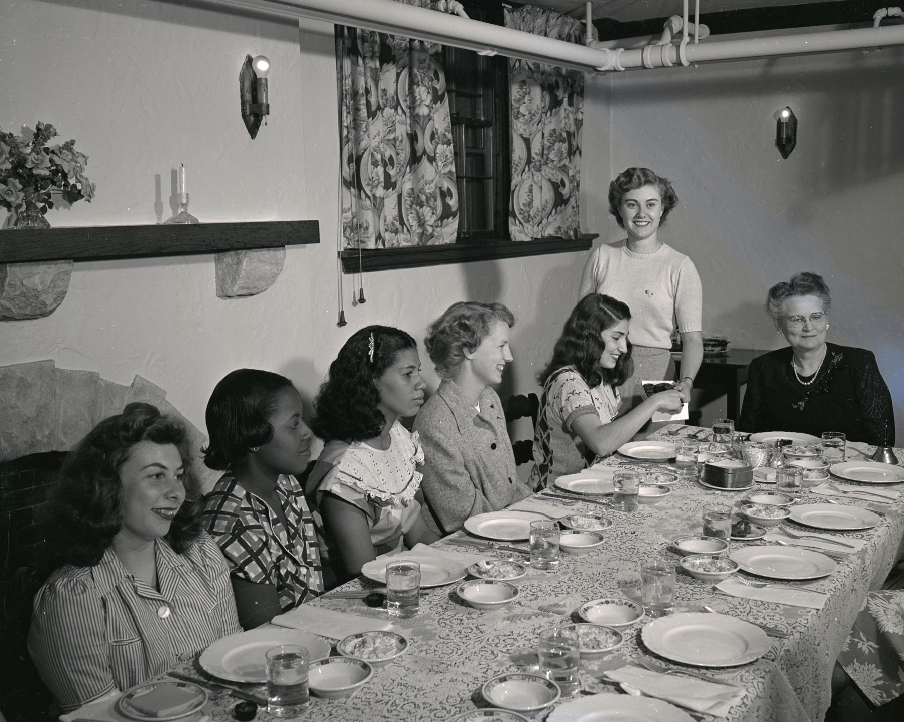 A black and white photograph of women around a dining table