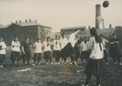 A black and white image of a woman throwing a ball outside while other women watch