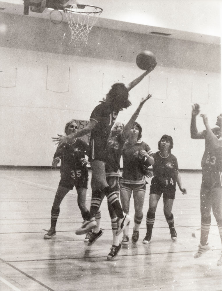 A black and white image of a woman jumping to shoot a basket