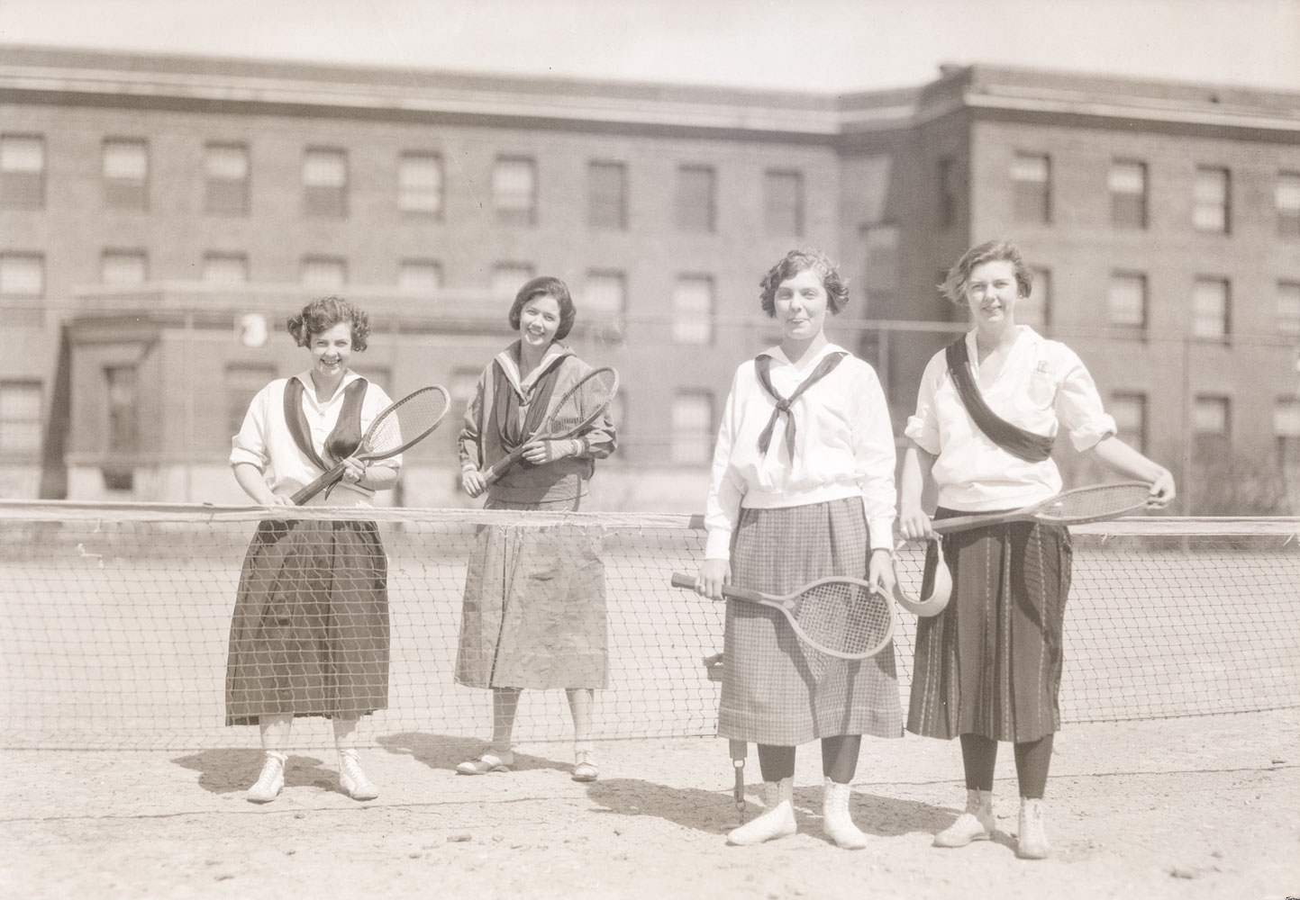 A black and white image of four women holding tennis rackets