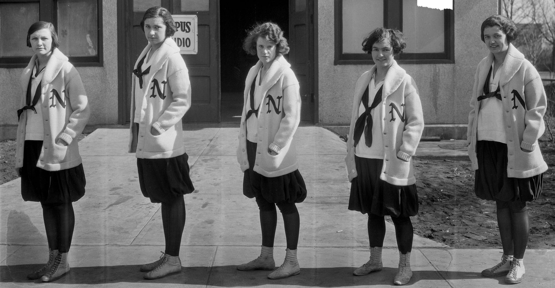 A black and white image of five women wearing coats with an N logo