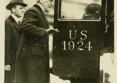 A black and white photograph of President Wilson opening an automobile door for Edith Wilson